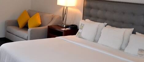 Habitación de hotel con cama, mesita de noche, lámpara, silla y dos almohadas.