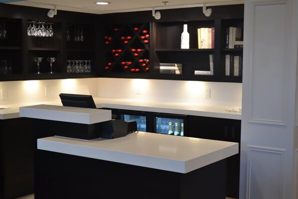 A modern kitchen with a white countertop and black cabinetry. There are wine glasses and bottles on the shelves.