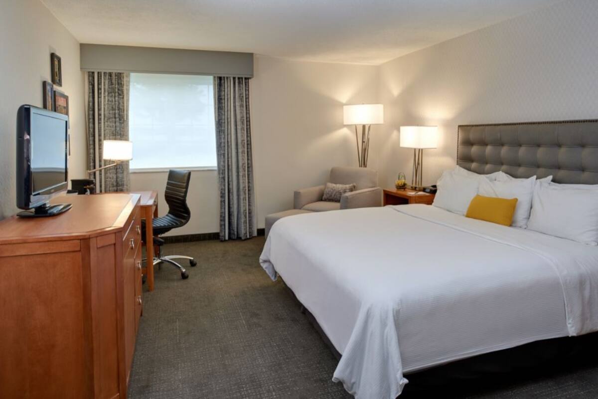 Une chambre d’hôtel comprenant un lit, un bureau avec un ordinateur, une chaise et deux lampes.