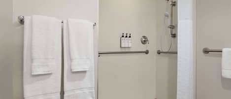 A shower area with a glass door, a towel rack with two towels, a handrail, and a small shelf with toiletries.