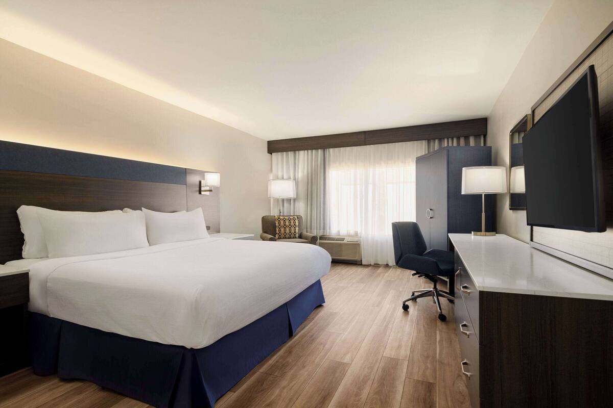 A hotel room with a large bed, a desk, a chair, and a flat-screen TV.