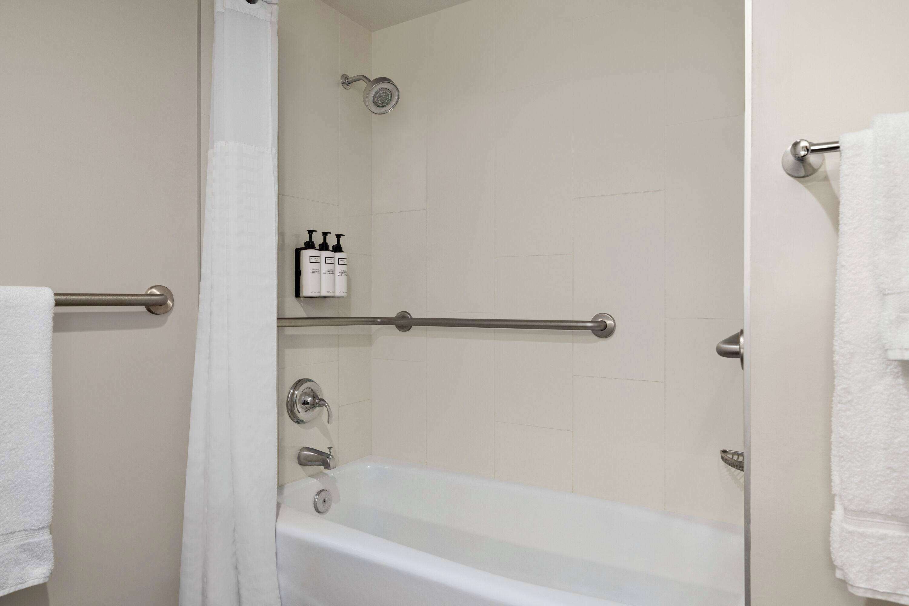 A bathroom with a bathtub, a shower, and a handrail. There are toiletries on the wall and a towel rack.