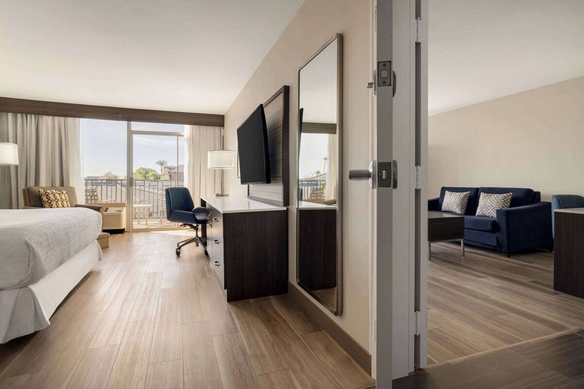 A hotel room with a bed, desk, chair, and a balcony with a view.
