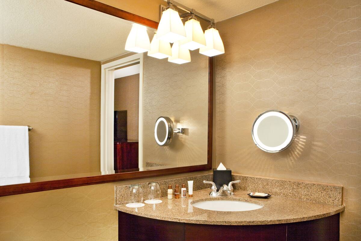 A bathroom with a granite countertop, a sink, a mirror, and a chandelier.