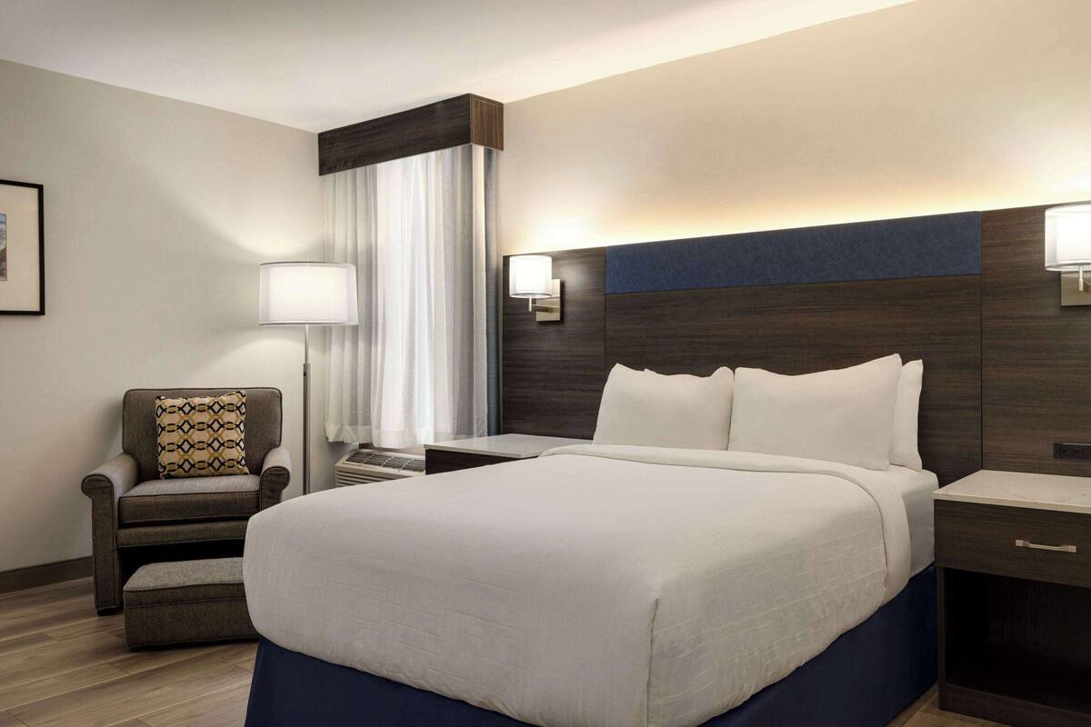A hotel room with a large bed, a chair, a desk, and a lamp.