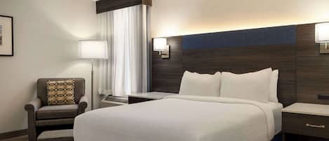 A hotel room with a large bed, a chair, a desk, and a lamp.
