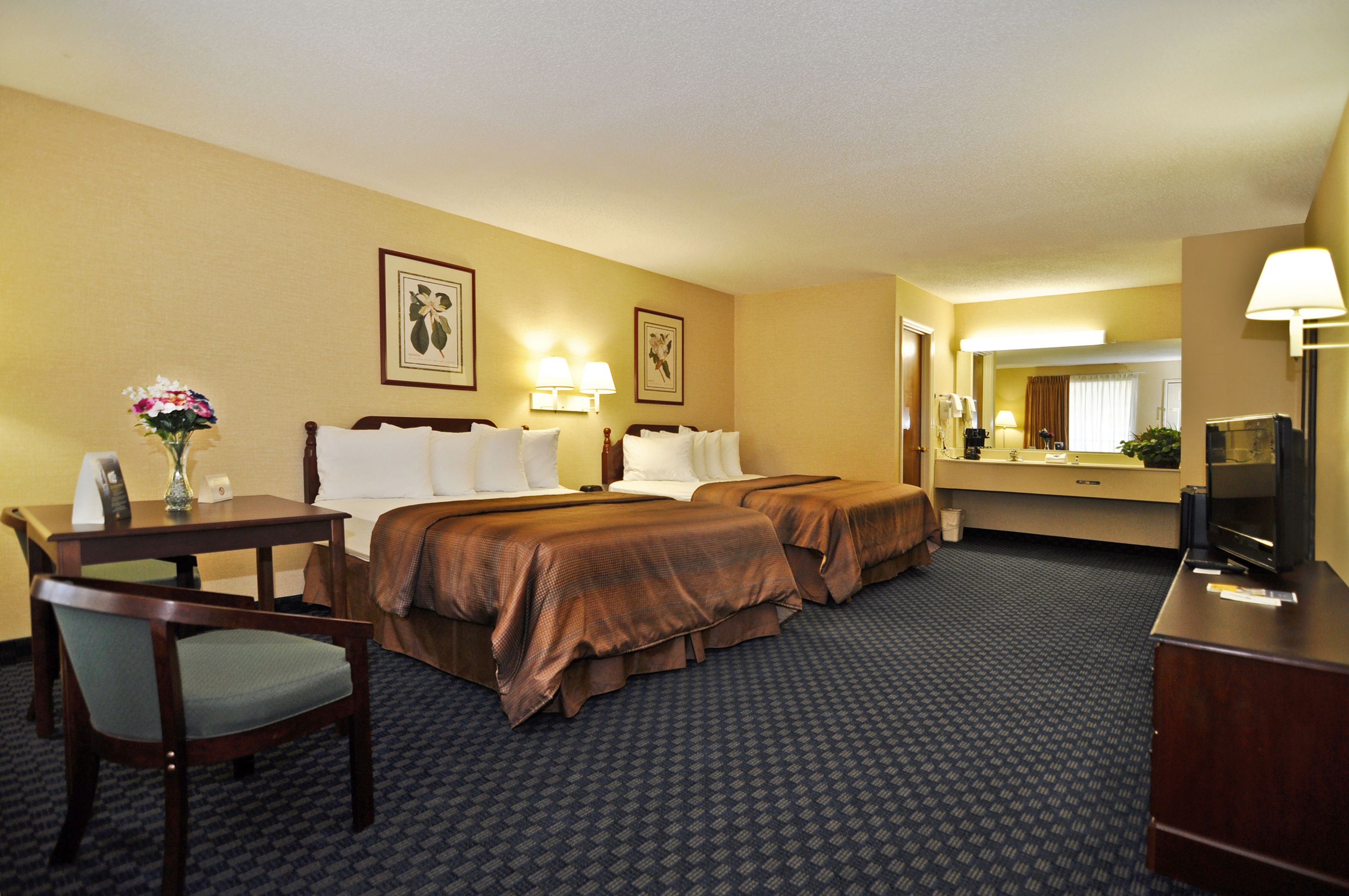 A hotel room with two beds, a desk, a chair, a TV, and a bathroom visible through an open door.