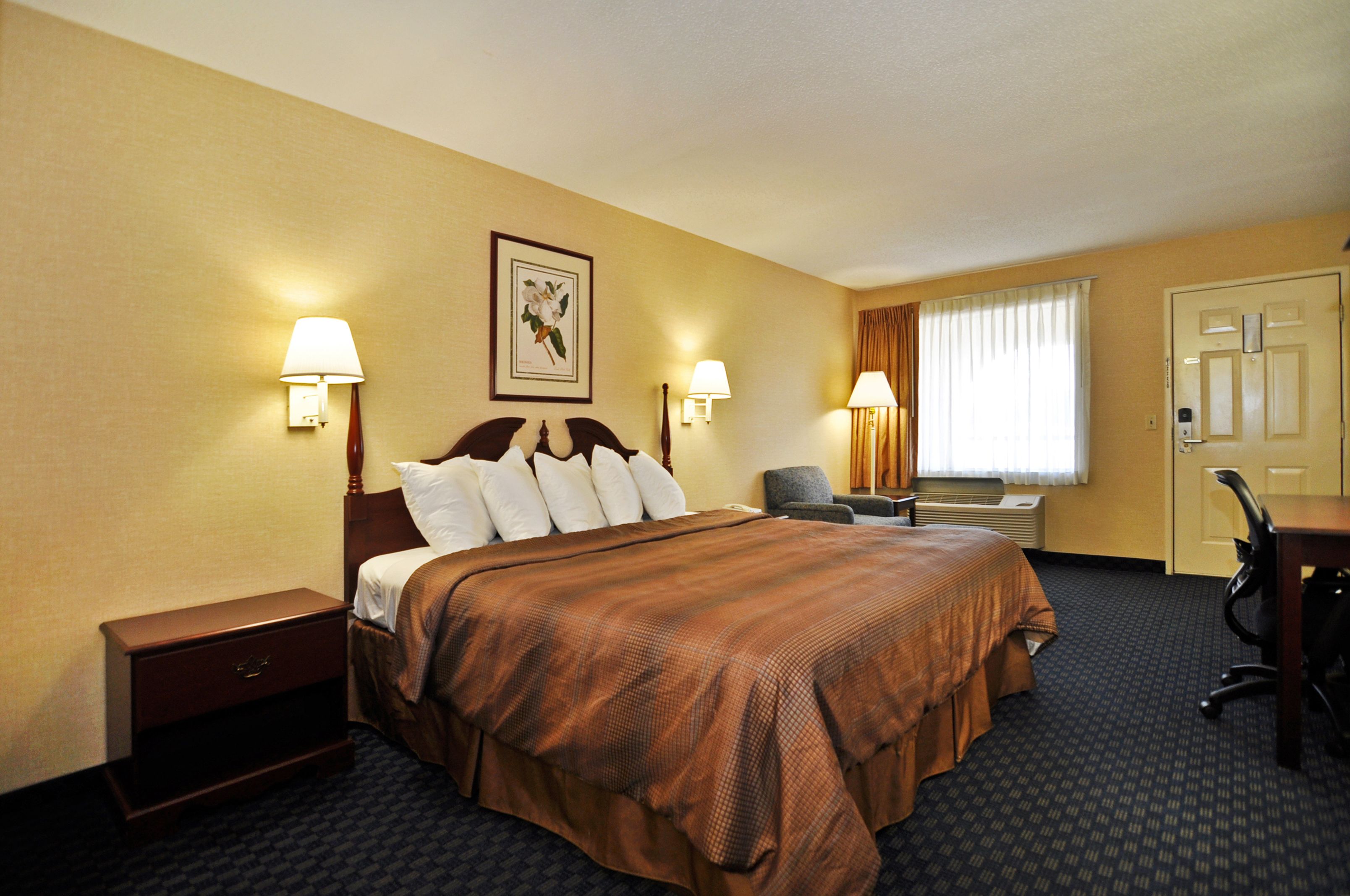 Ein Hotelzimmer mit einem großen Bett, zwei Nachttischen, einem Schreibtisch und einem Stuhl.