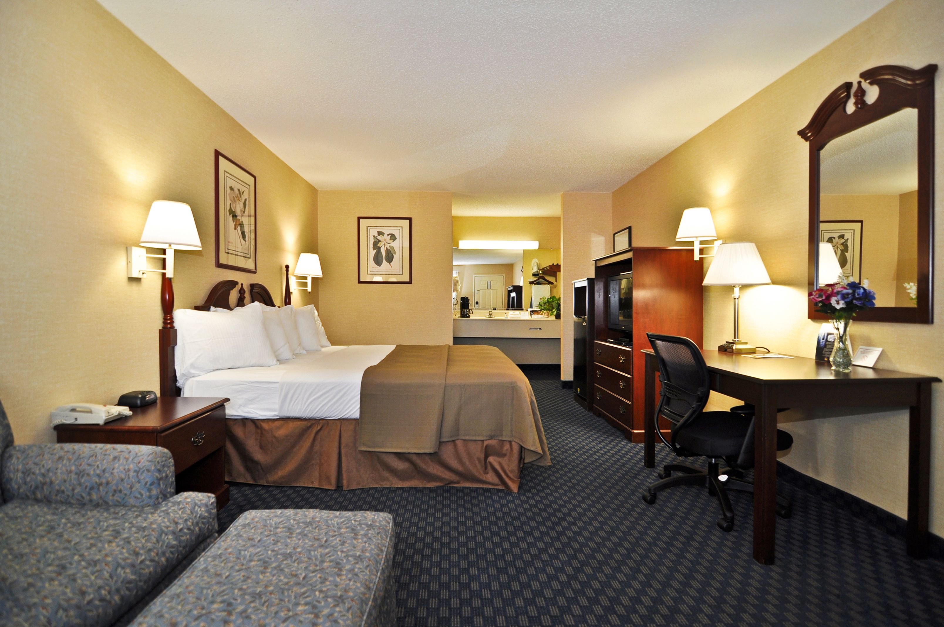 A hotel room with a bed, two bedside tables, a desk with a chair, a dresser, and a large mirror.