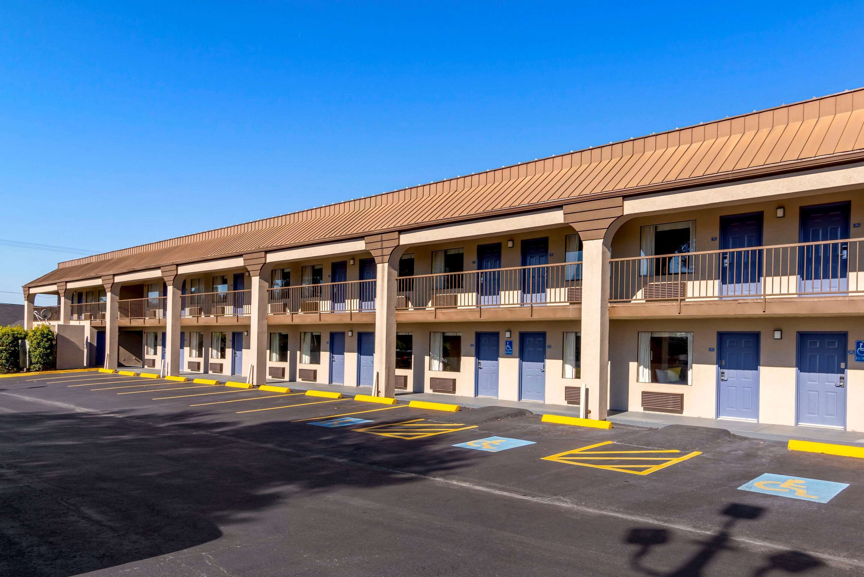 Un motel doté de nombreux balcons, un parking avec des places réservées aux personnes handicapées et un ciel d’un bleu éclatant.