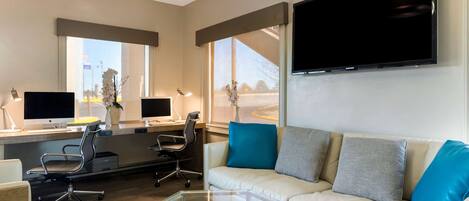 A modern living room with a sofa, glass coffee table, and two desks with computers.