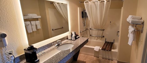 A modern bathroom with a granite countertop, a large mirror, a shower with a glass door, and multiple towel racks.