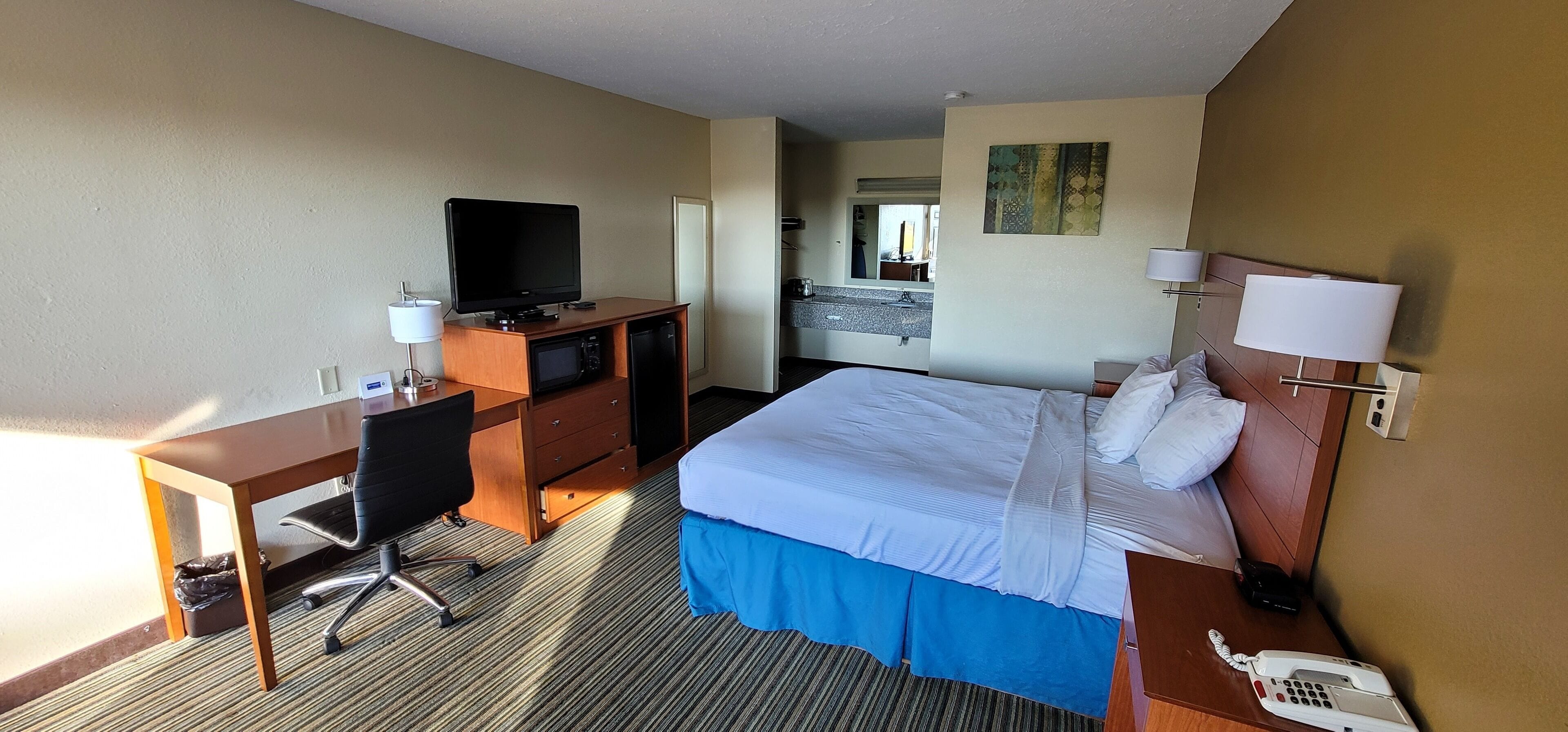 A hotel room with a bed, desk, chair, television, and a telephone.