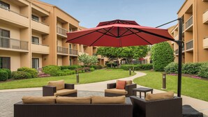 Une cour avec des sièges en plein air, un parasol rouge et un bâtiment doté de balcons.
