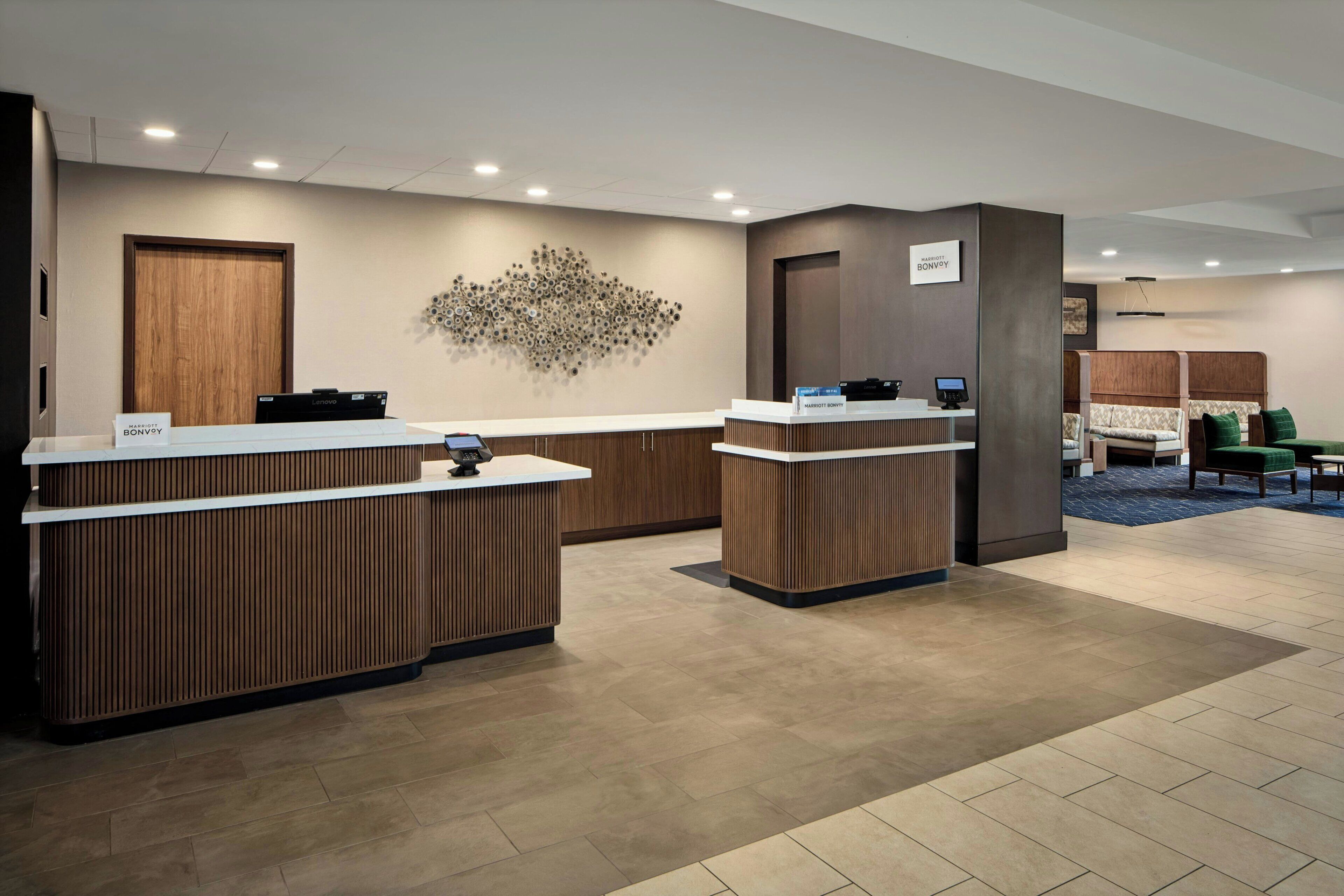 Een hotel receptie met twee balies, een decoratief object aan de muur en een zithoek met een bank en stoelen.