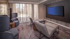 Un salon moderne avec un téléviseur à écran plat fixé au mur, une grande fenêtre ornée de rideaux légers et une moquette à motifs.