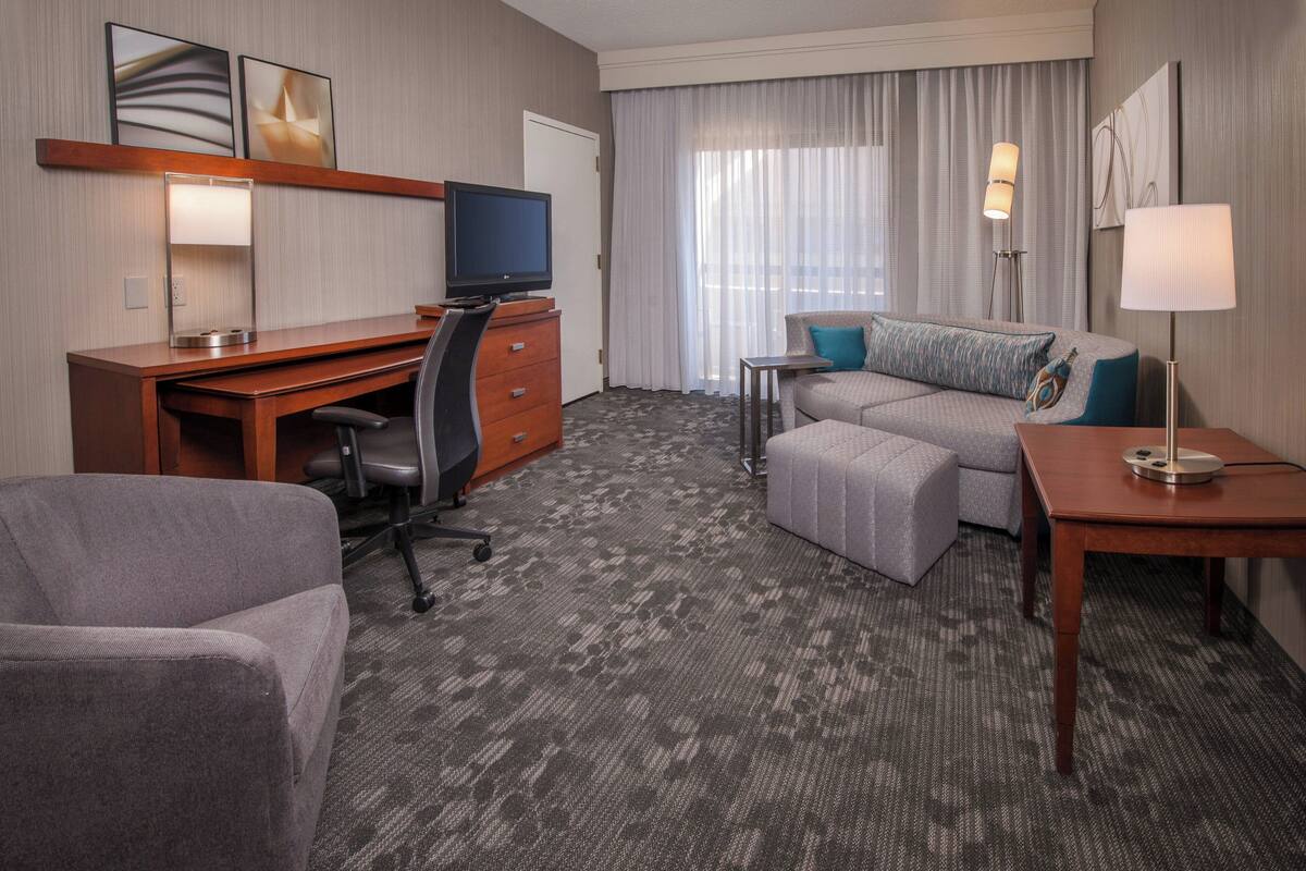 A hotel room with a desk, a comfortable sofa, a small table, and a television.