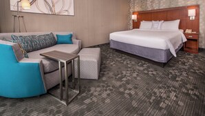 Une chambre d’hôtel avec un lit, un canapé, une petite table et une table de chevet avec une lampe.