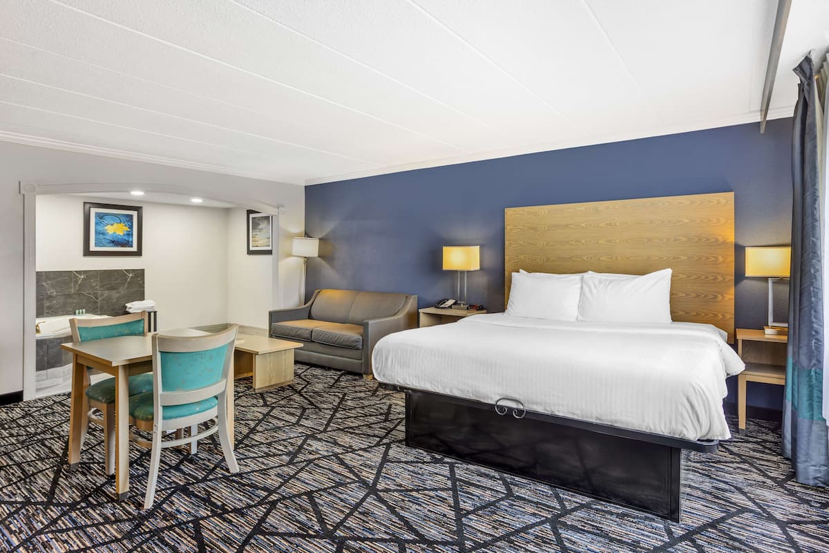 A hotel room with a large bed, a desk with a chair, a sofa, and two bedside lamps.