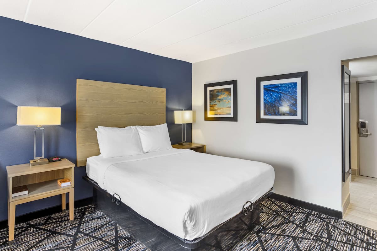A hotel room with a large bed, two bedside tables with lamps, a headboard, and two framed pictures on the wall.