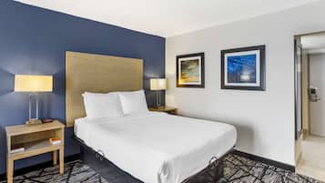 A hotel room with a large bed, two bedside tables with lamps, a headboard, and two framed pictures on the wall.