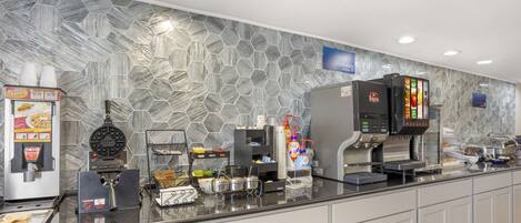 A buffet area with a variety of food stations, including a waffle maker, coffee machines, and a refrigerated display.