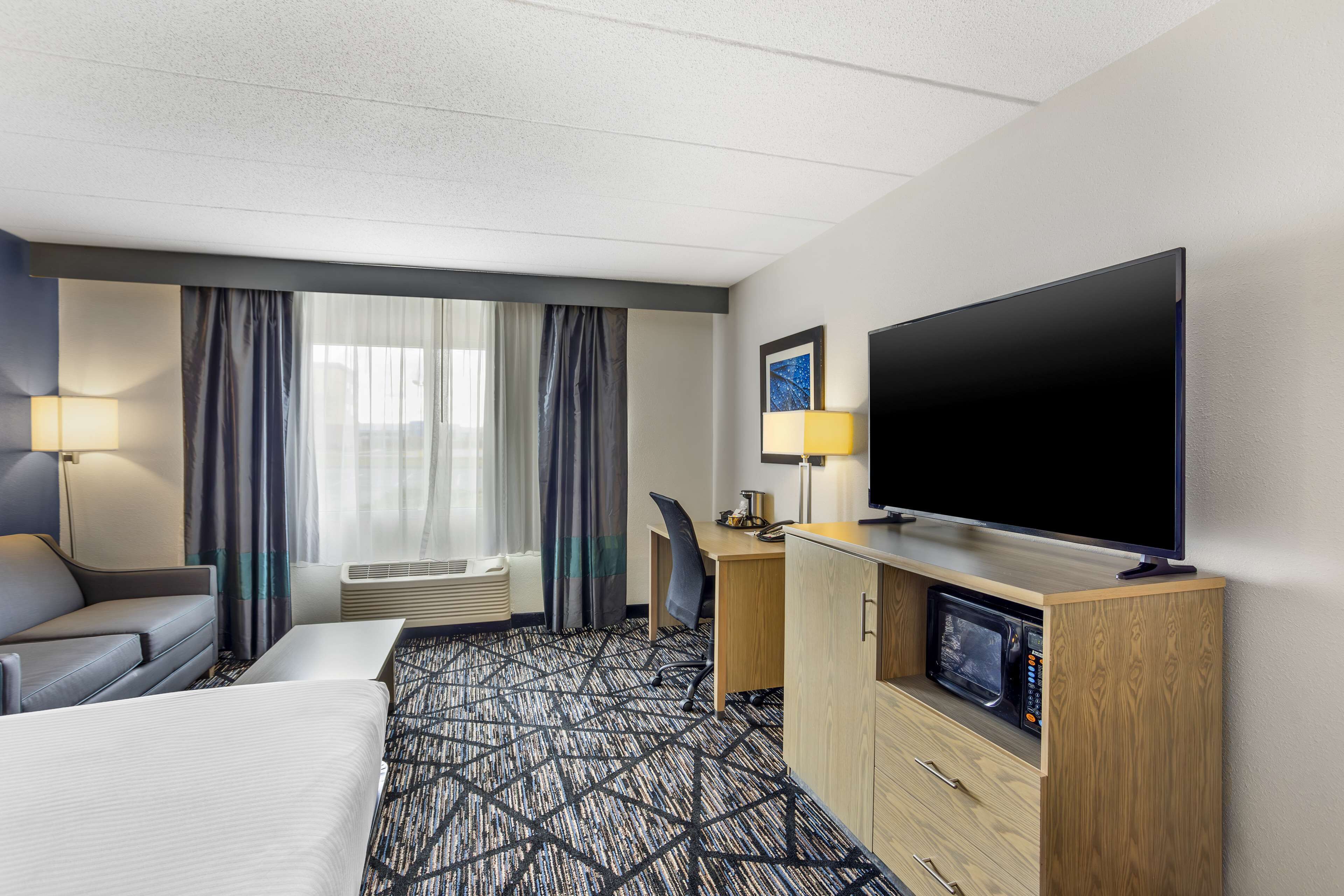 A hotel room with a large bed, a desk, a television, and a microwave.