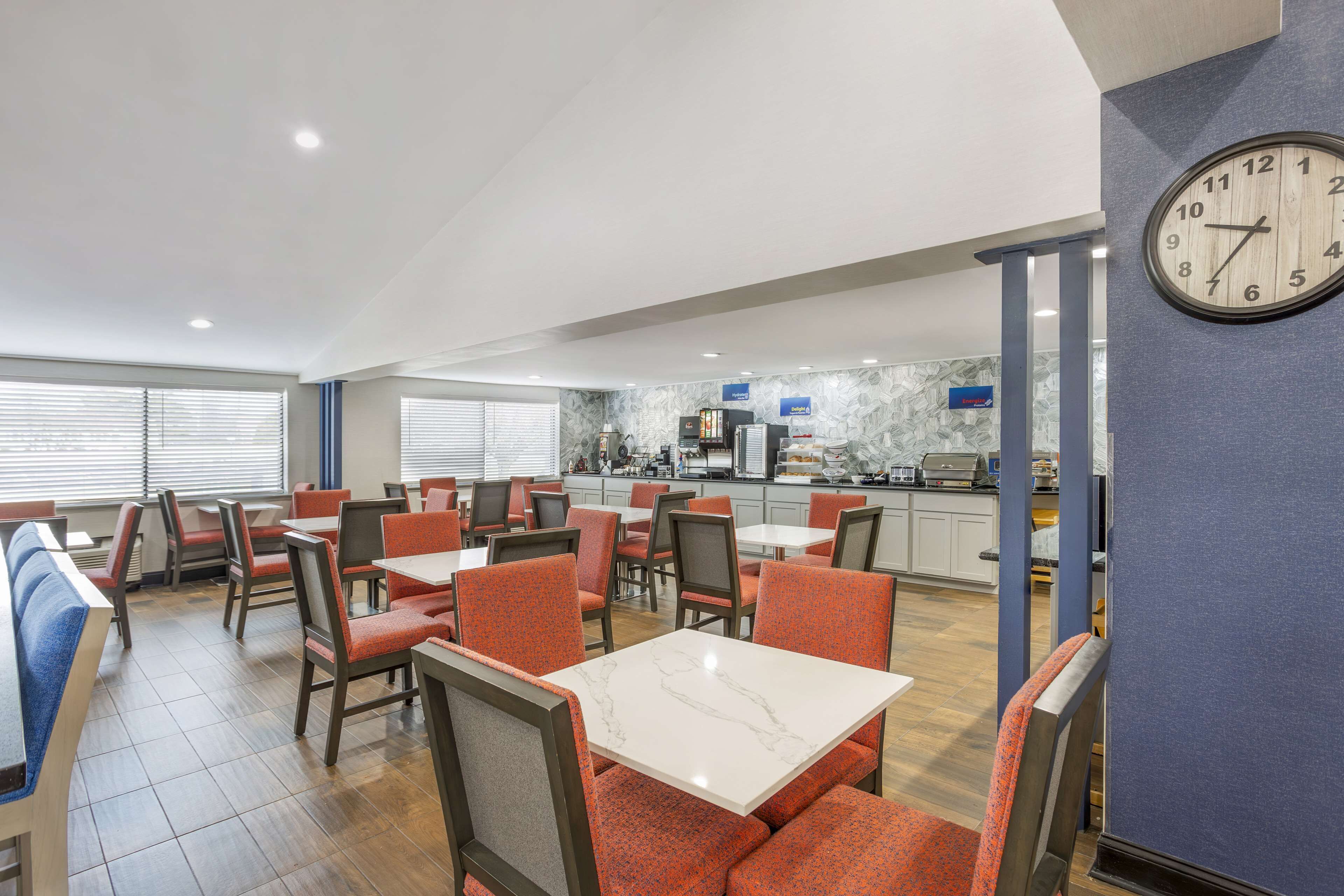 En restaurant i et hotel med siddepladser i båse og ved borde, et køkken i baggrunden og et ur på væggen.