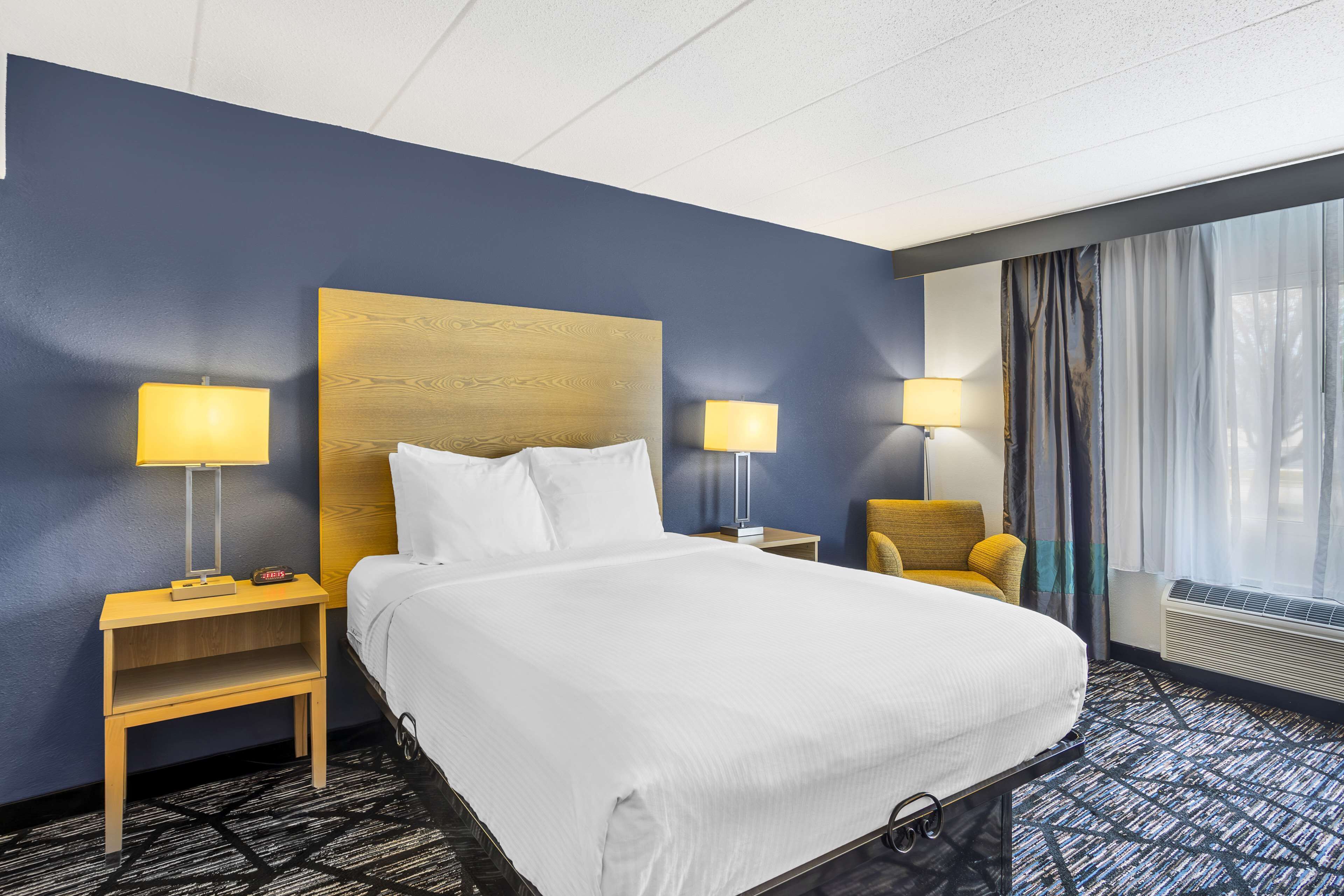 A hotel room with a large bed, two bedside tables with lamps, a chair, and a window with curtains.