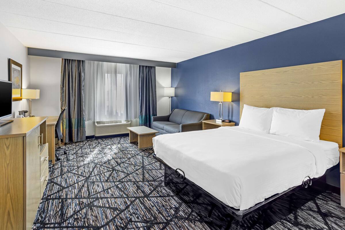 A hotel room with a large bed, a desk, a chair, and a TV.