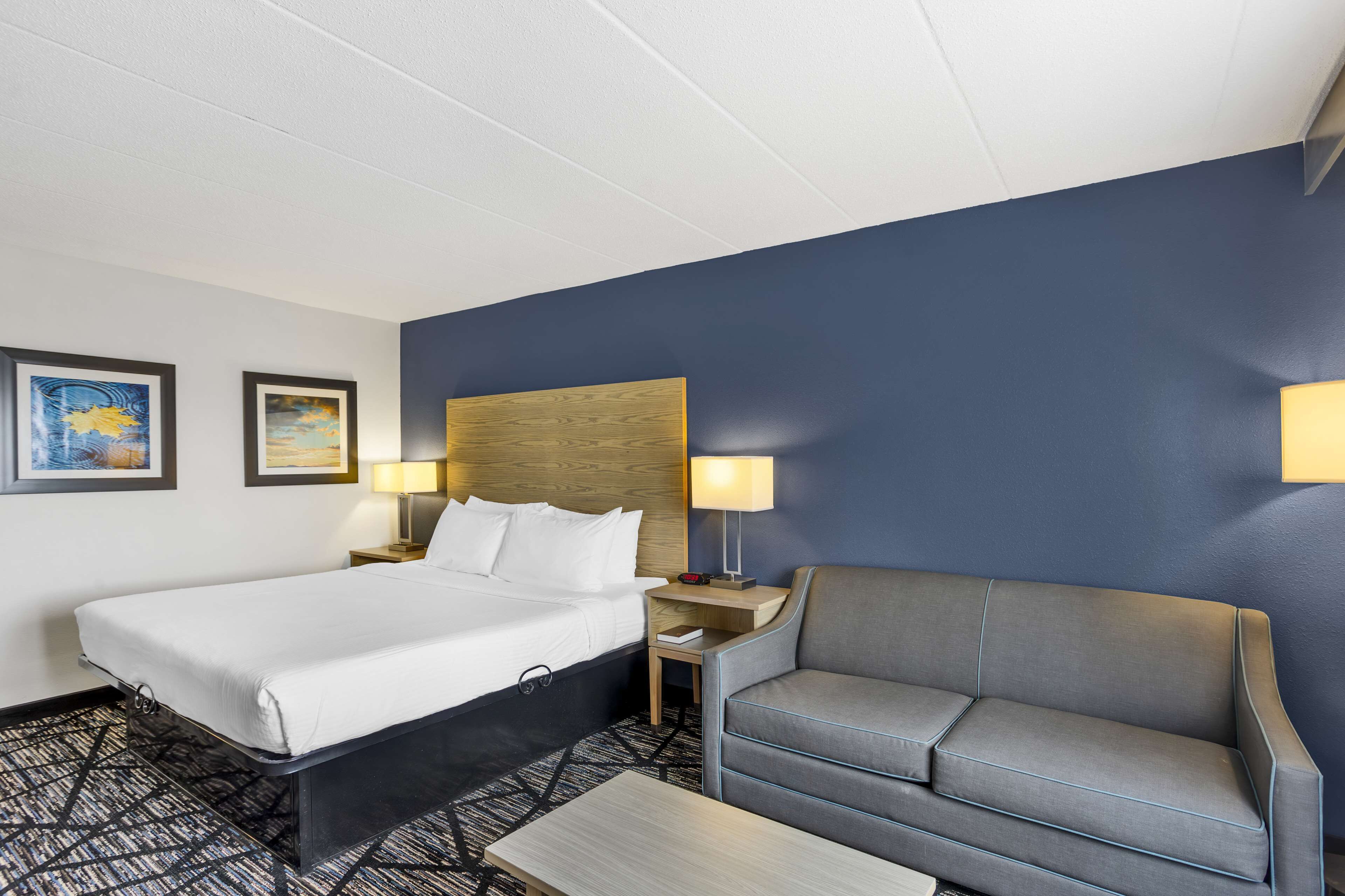 A hotel room with a bed, a gray sofa, a small table, and two wall-mounted lamps.