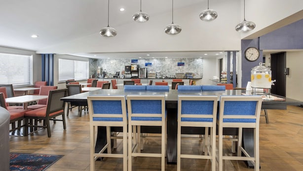 A modern dining area with multiple tables and chairs, a kitchen in the background, and pendant lighting. - Best Western Westgate Inn (York)