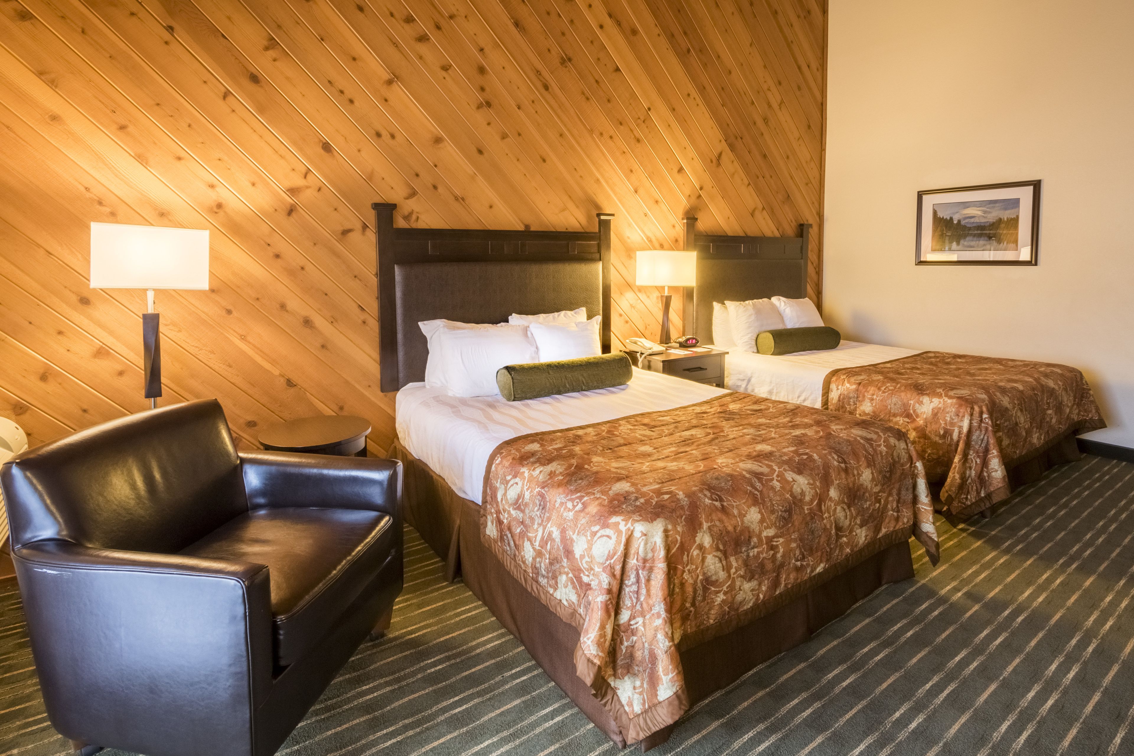 A hotel room with two beds, a leather armchair, and a wooden ceiling.