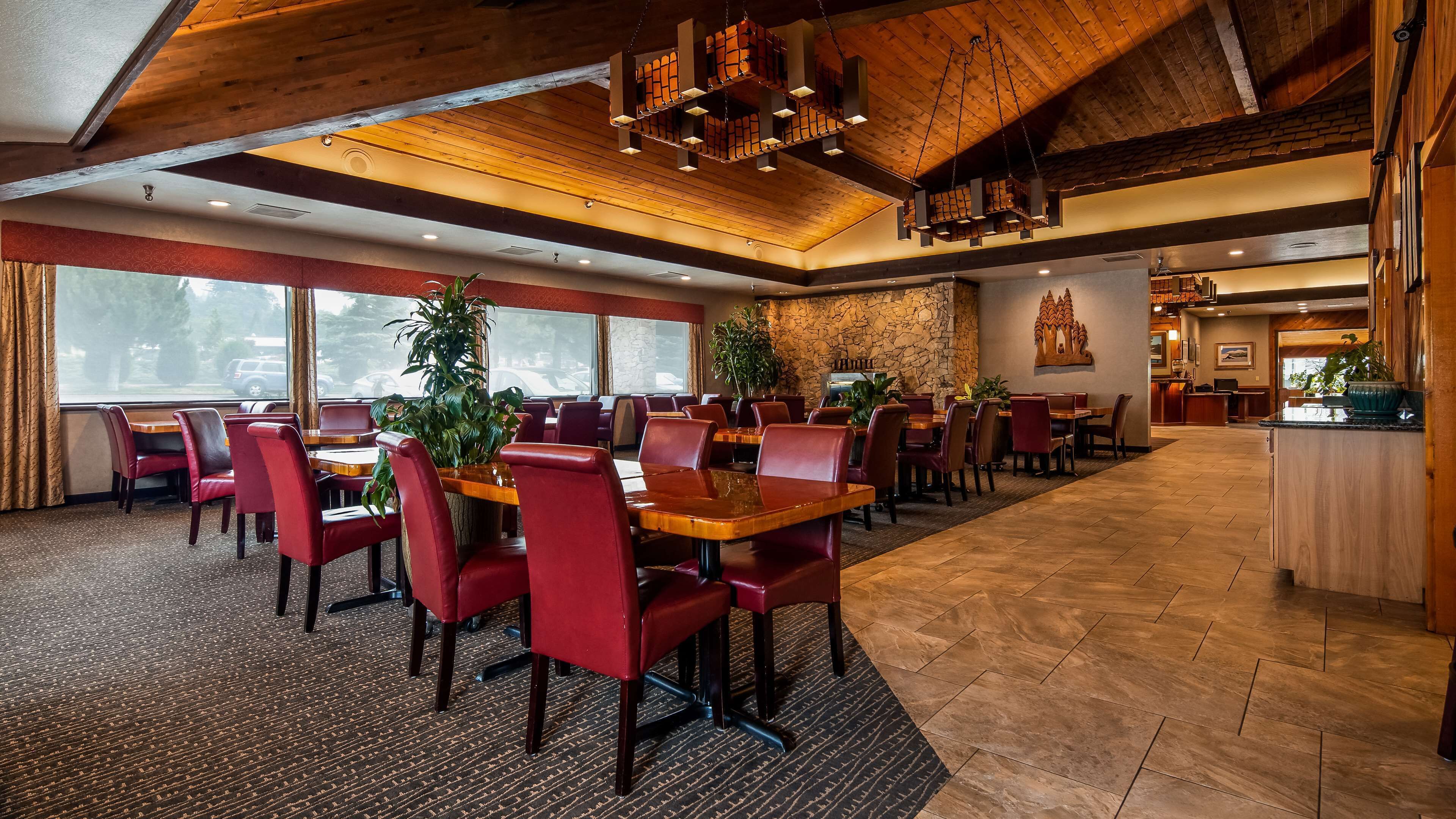 A spacious restaurant with high ceilings, wooden beams, and a mix of red and brown chairs.