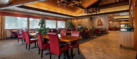 A spacious restaurant with high ceilings, wooden beams, and a mix of red and brown chairs.