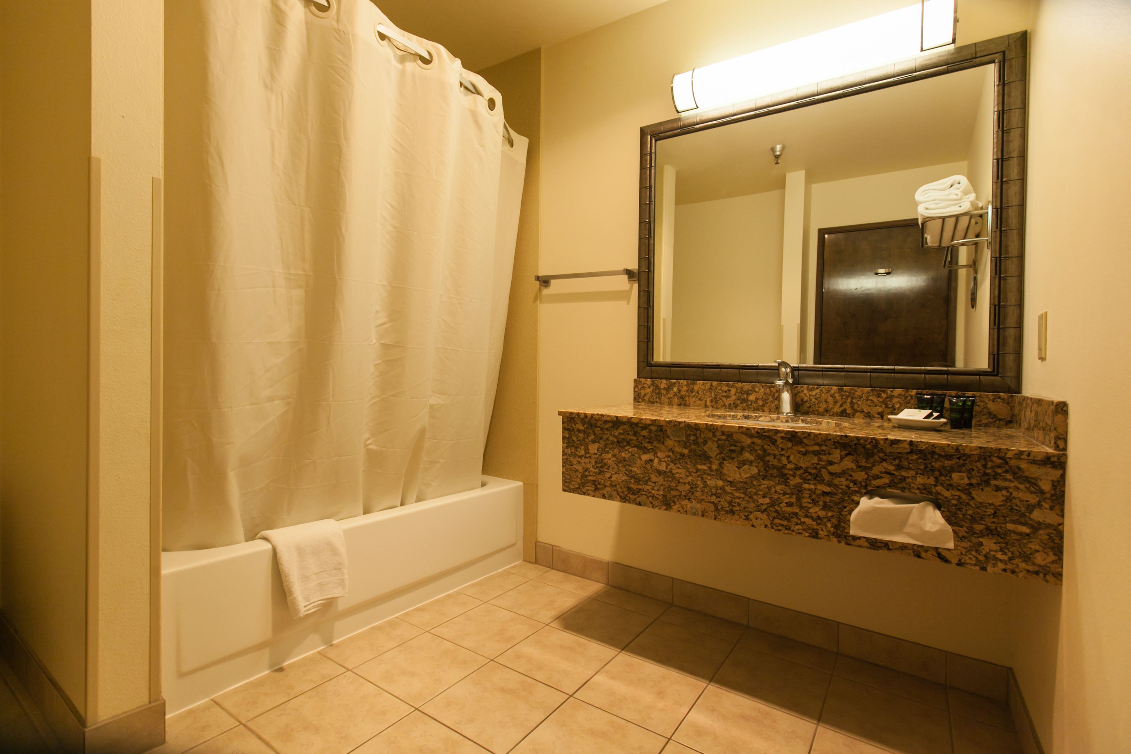 A bathroom with a bathtub, a sink with a granite countertop, and a mirror above the sink.