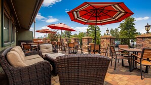 An outdoor patio with wicker furniture and red umbrellas, stone pillars, and a view of the street. - Best Western Plus Tree House (Mount Shasta)
