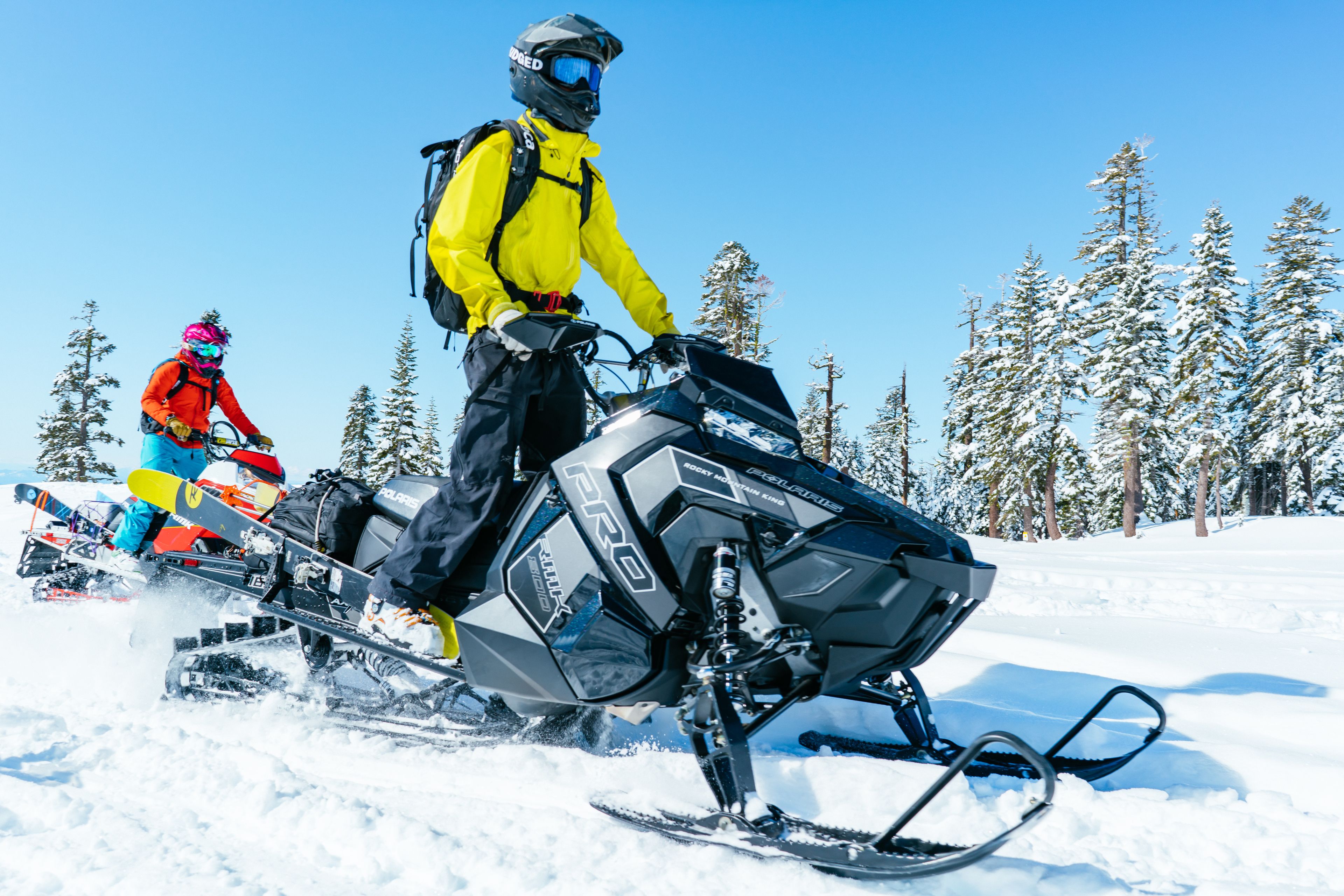 A snowmobile with a rider in a yellow jacket and black helmet.