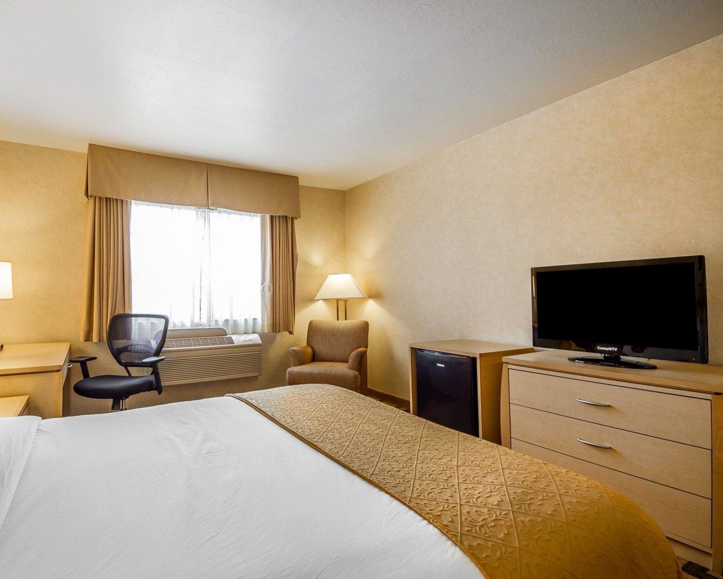 Habitación de hotel con una cama, un escritorio con computadora, una silla, un televisor y una lámpara.
