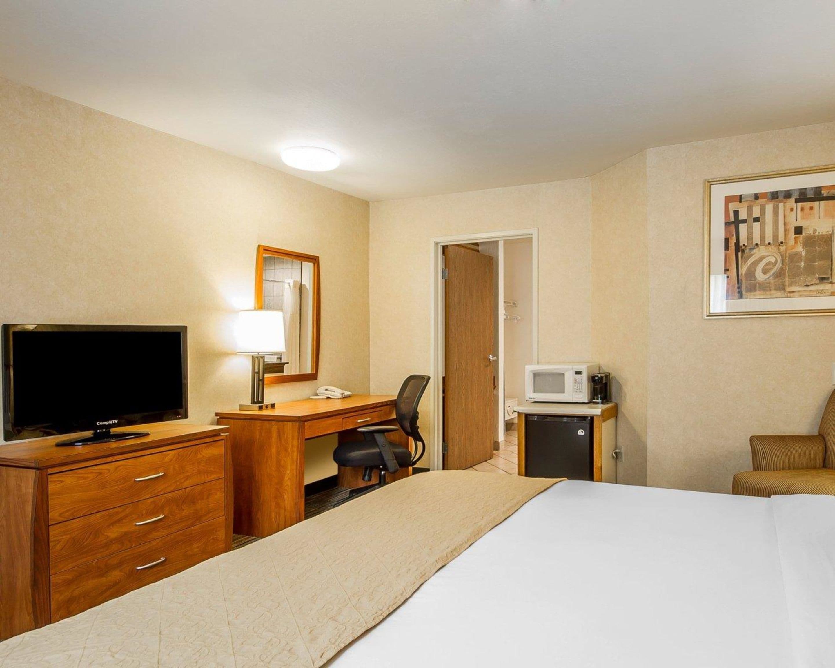 Ein Hotelzimmer mit einem Bett, einem Schreibtisch mit Fernseher, einem Sessel, einer Mikrowelle und einer Tür.