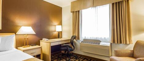 Habitación de hotel con cama, escritorio, silla y un ventanal con cortinas.