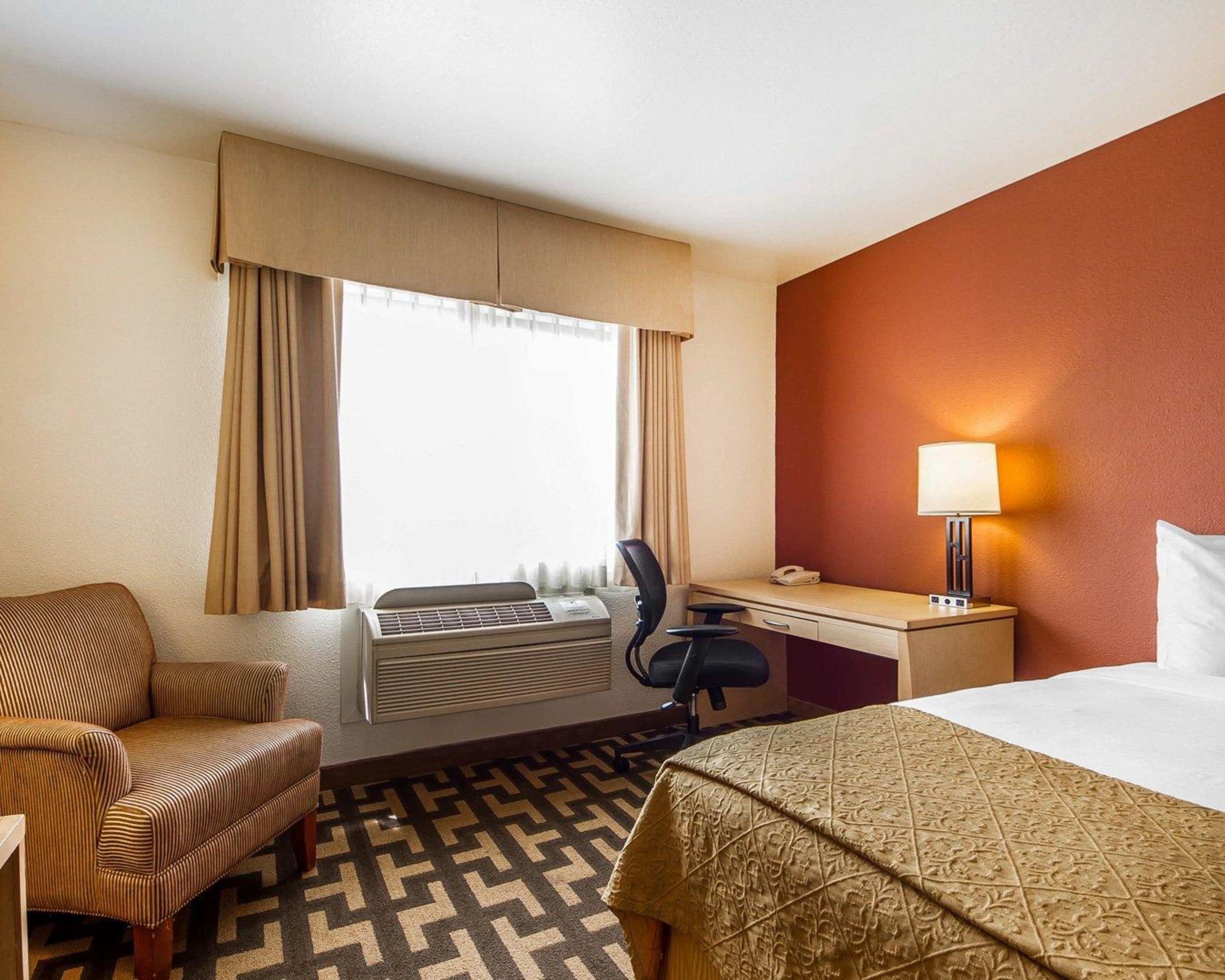 A hotel room with a bed, a desk, a chair, an air conditioner, and a window with curtains.