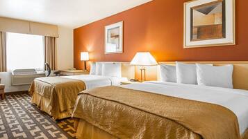A hotel room with two beds, a desk, a chair, and a window with curtains.