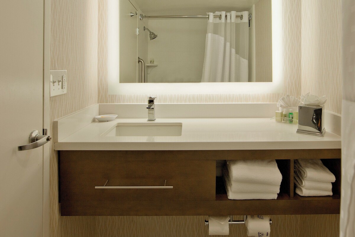 Une salle de bain avec un lavabo blanc, un miroir, une douche et un porte-serviettes.