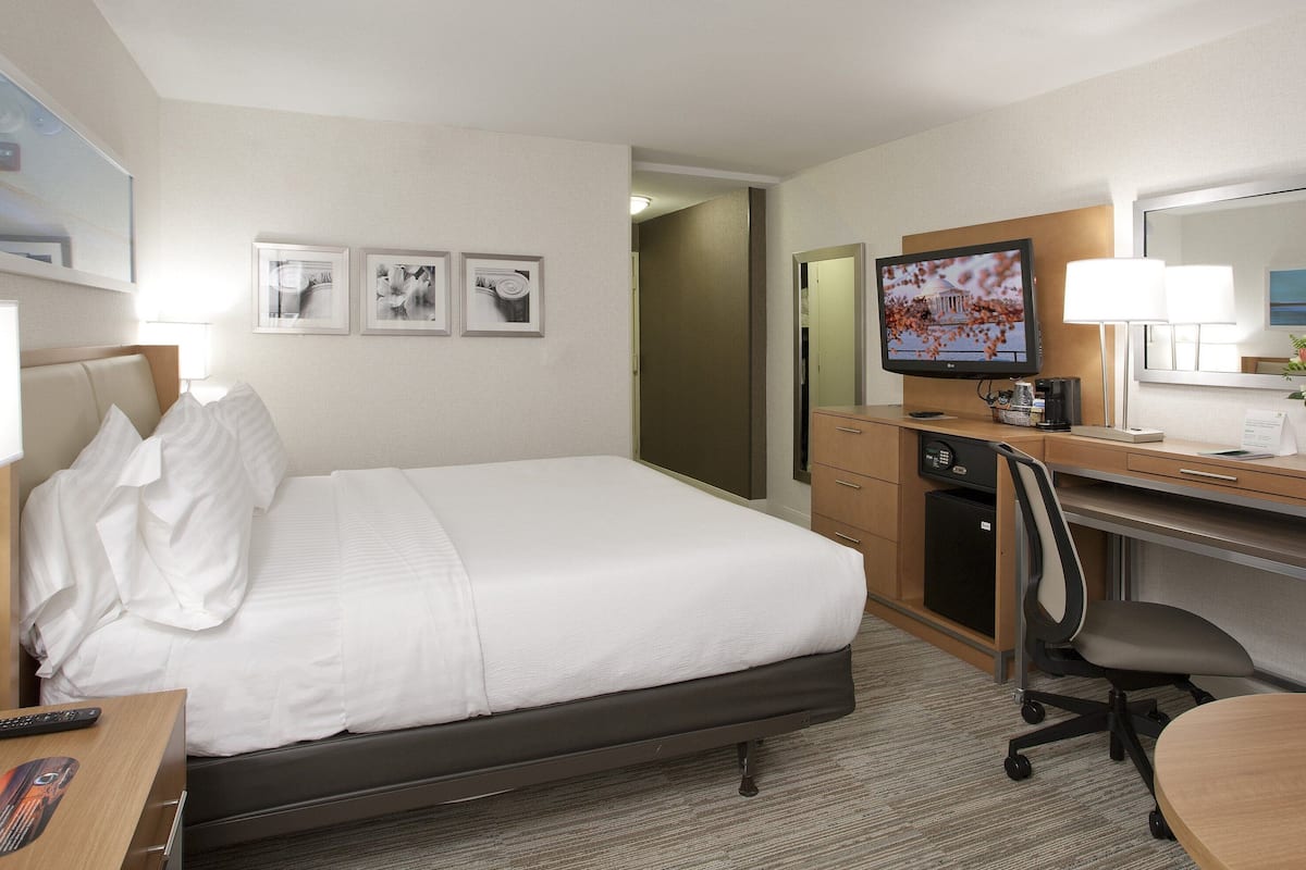 Habitación de hotel con cama, escritorio, silla, televisor y una pequeña cocina.