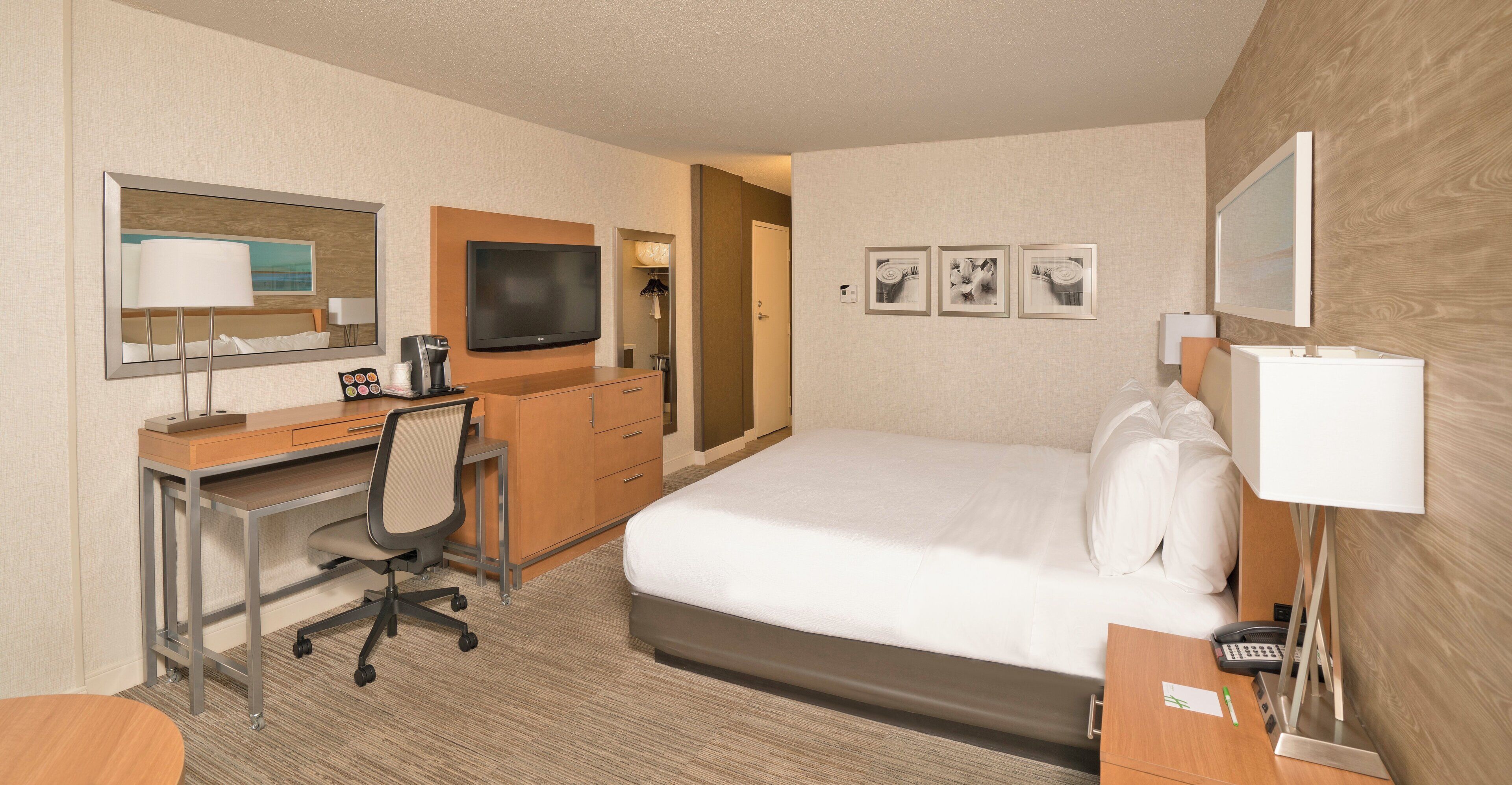 Habitación de hotel con cama, escritorio, silla, televisor y una obra de arte en la pared.