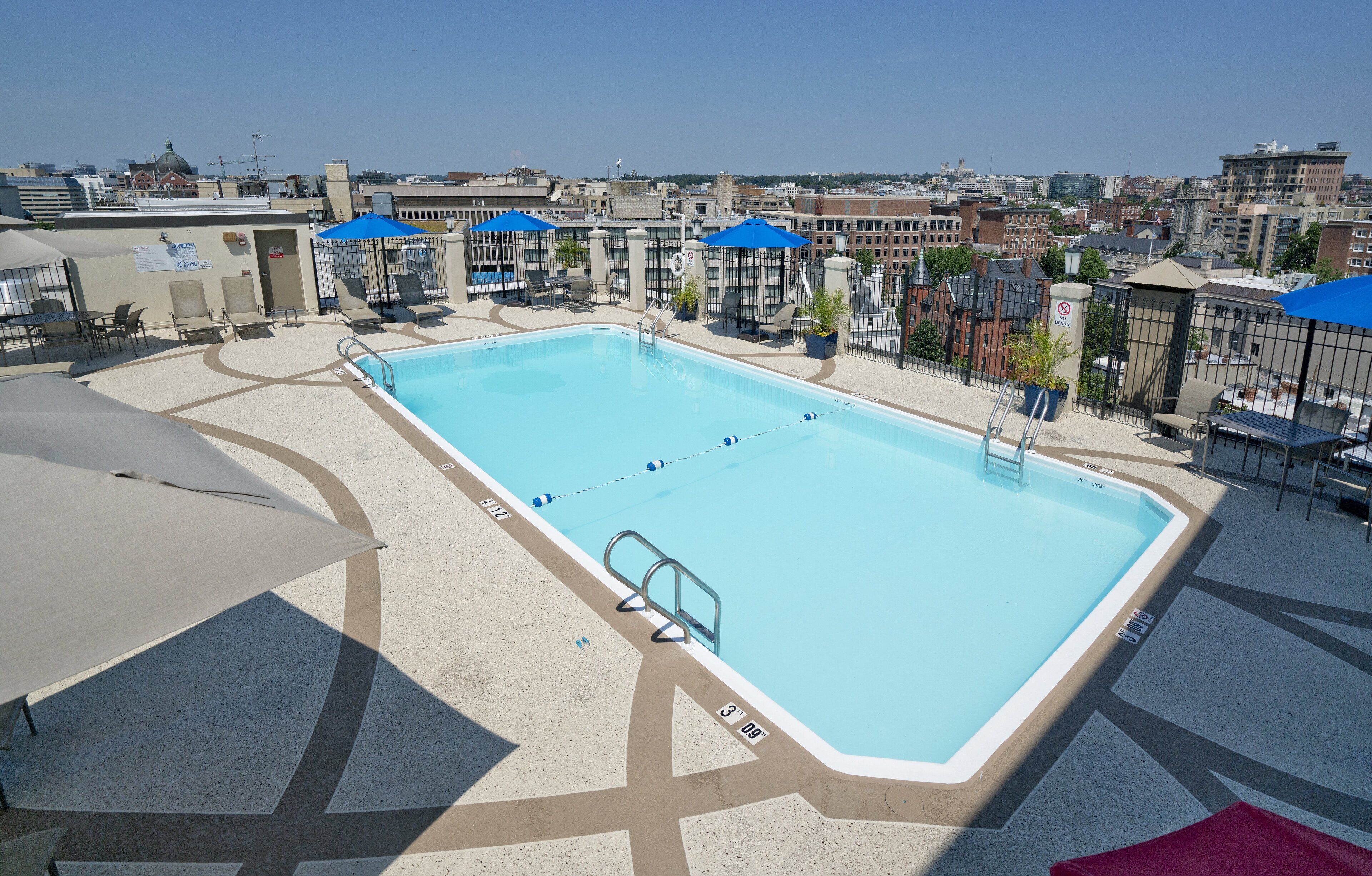 A rooftop swimming pool with lounge chairs and umbrellas, surrounded by buildings.