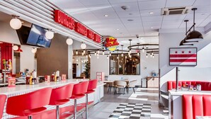 A modern restaurant interior with red bar stools, a checkered floor, and a red and white striped wall decoration. - Holiday Inn Washington-Central/White House by IHG (Washington)