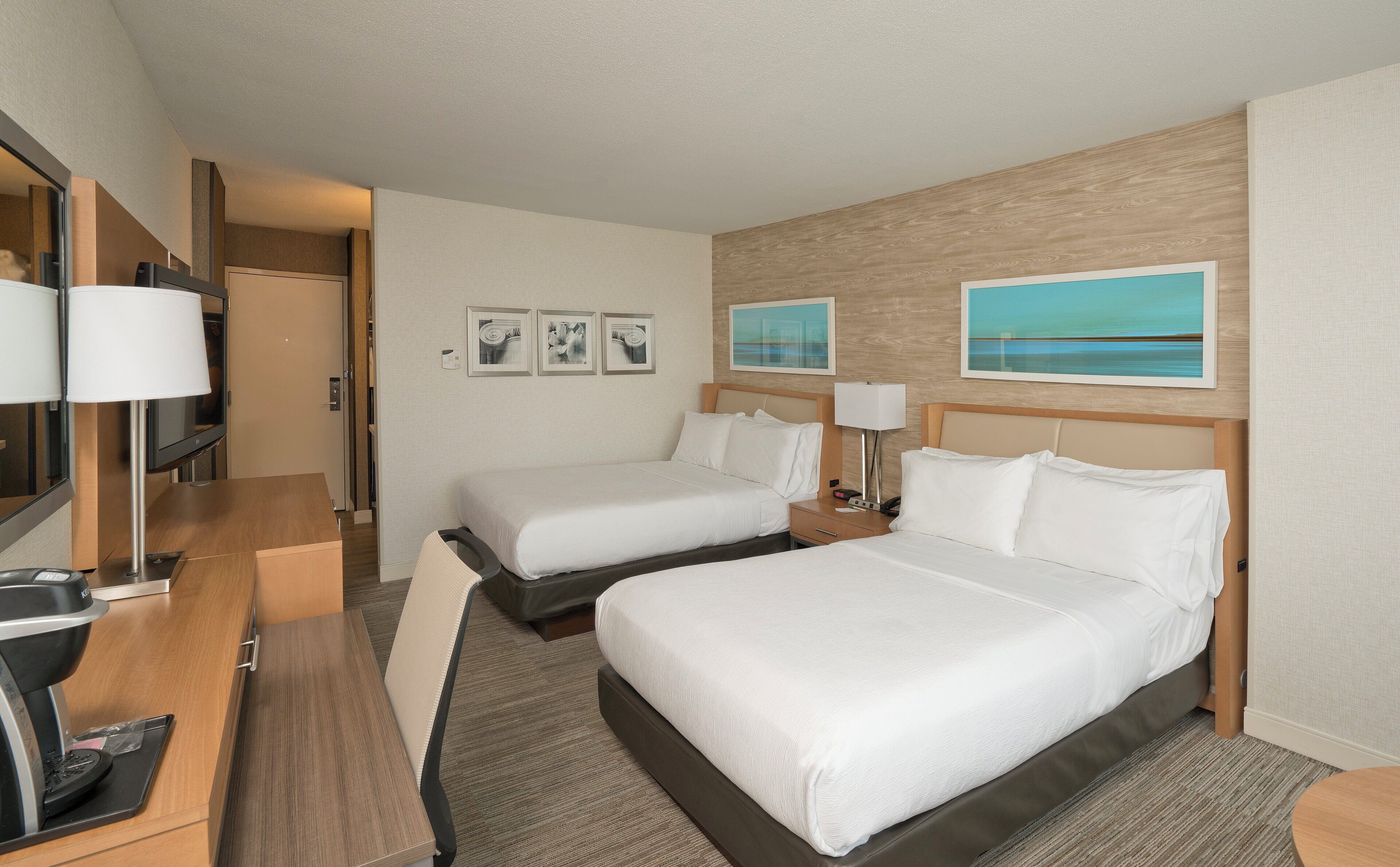 Ein Hotelzimmer mit zwei Betten, einem Schreibtisch, einem Fernseher und Bildern an den Wänden.