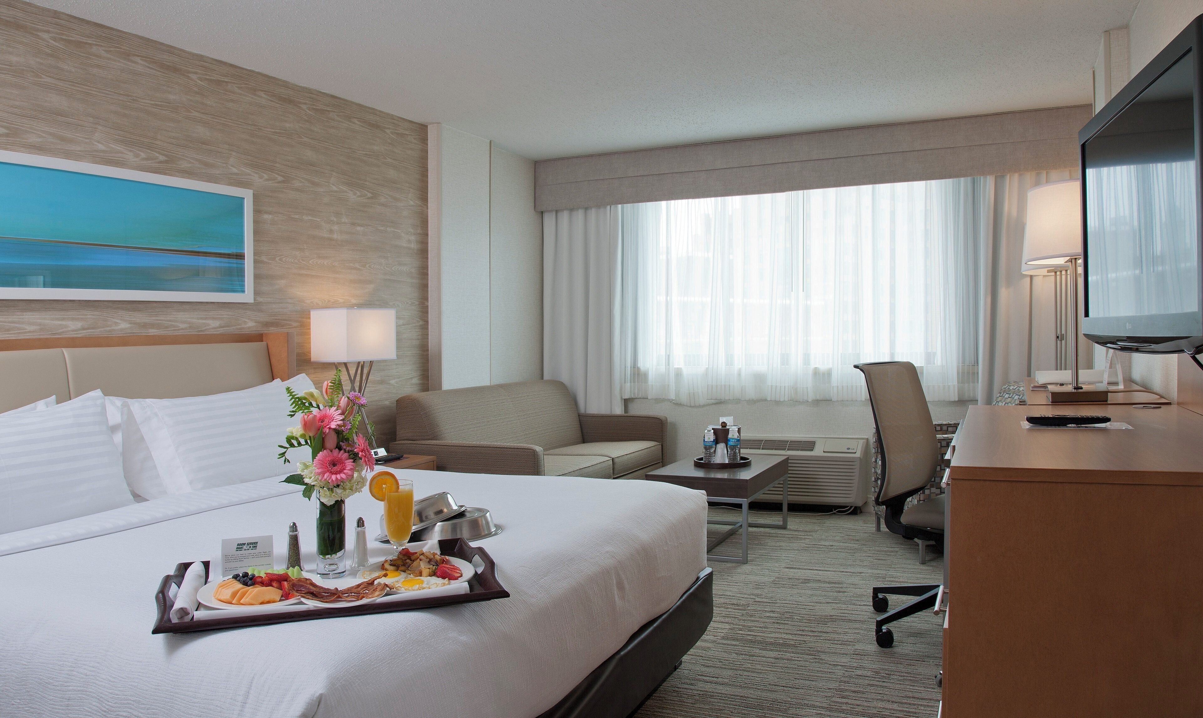 A hotel room with a bed, a desk, a chair, a TV, and a window with curtains.